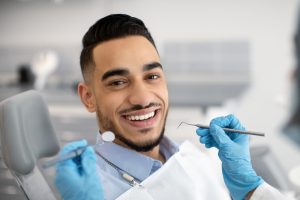 patient smiling as dentist evaluates his smile with dental tools